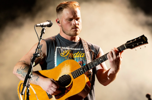 Zach Bryan performing on stage (photo soruce from Nile West News) 